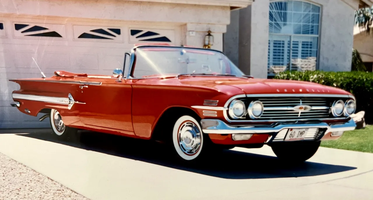 A red 1960 Chevrolet Impala convertible with the top down, parked on a driveway