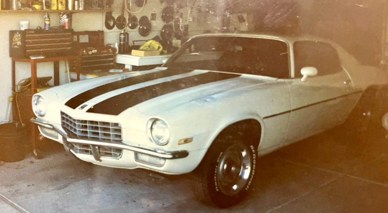 A white second-generation Chevrolet Camaro with black hood stripes, in a home garage