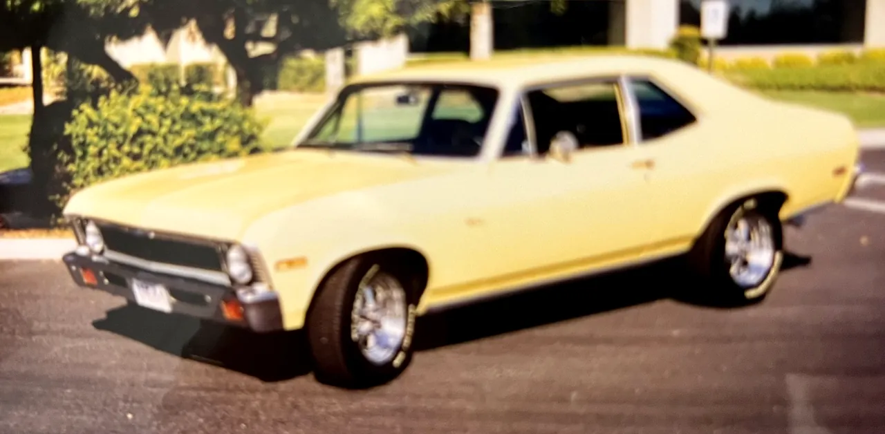 A yellow Chevrolet Nova two-door on chrome wheels, parked at the curb