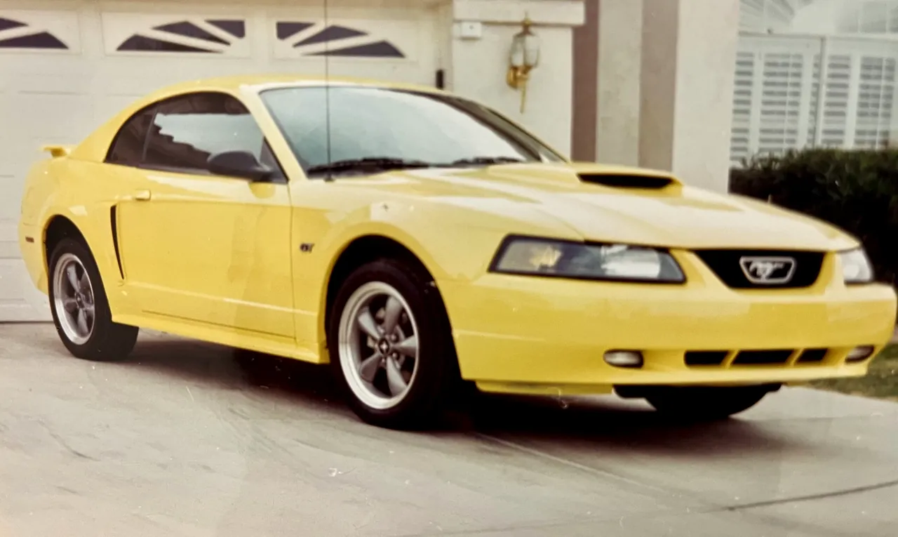 A yellow Ford Mustang GT parked in front of a garage